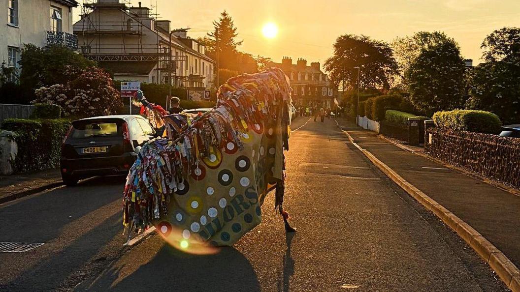 A hobby horse covered in colourful rags dancing down a street in Somerset at dawn, to mark May Day