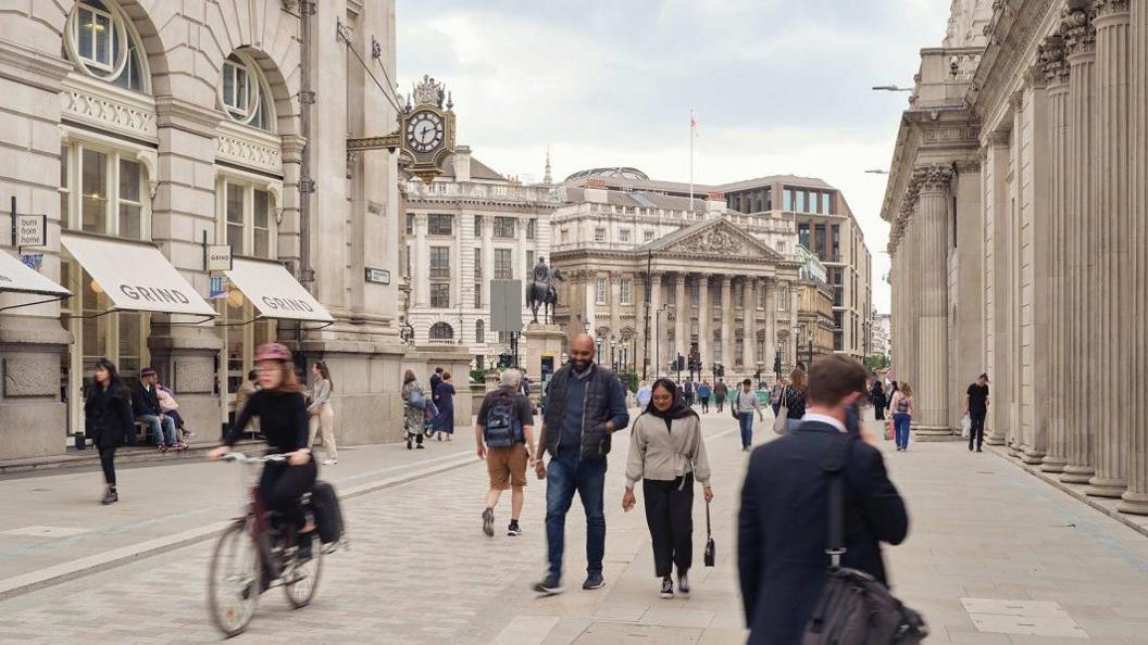 People walking in the middle of the road along Threadneedle Street. A cyclist also passes by.