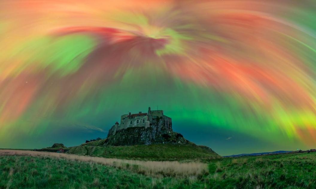 An array of green yellow and red bands of light illuminate the sky above a castle on a small hill.