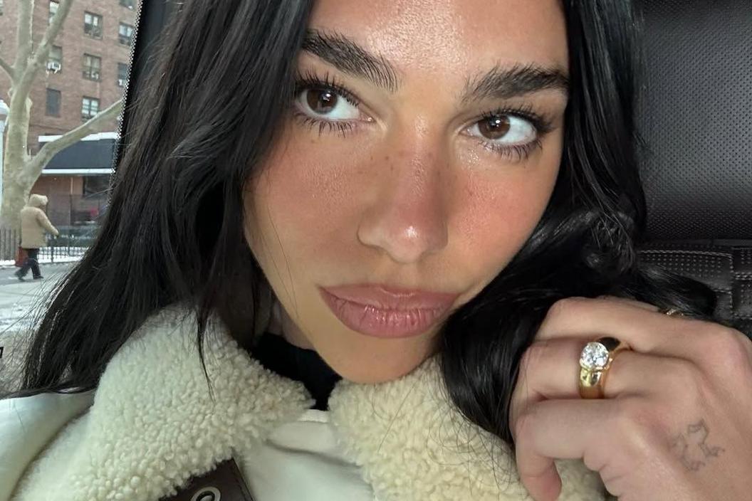 Selfie image of Dua Lipa, where her left hand is on show with her engagement ring - a thick gold band with a diamond in the centre - on show.