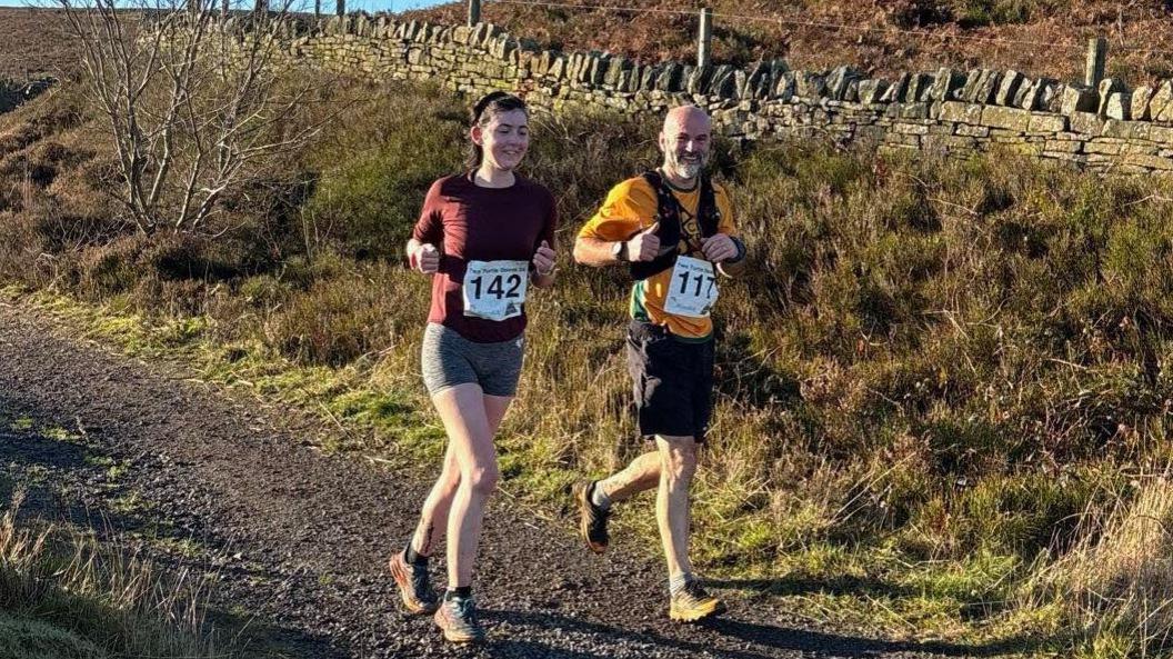 Ella Burns runs along a country track with her father Nick. Ella wears running number 142, while Nick has 117.