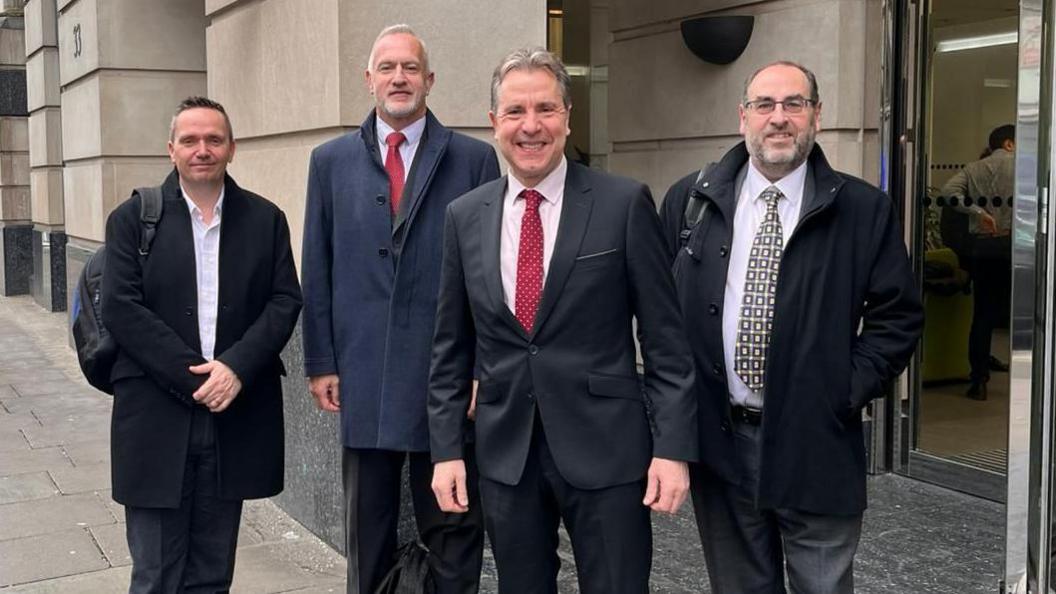 Standing outside the Department for Transport in London are North Somerset Council leader Mike Bell, South Gloucestershire Council leader Ian Boulton, Metro Mayor Dan Norris, and Bristol City Council leader Tony Dyer. All four men are smiling at the camera and wearing dark suits