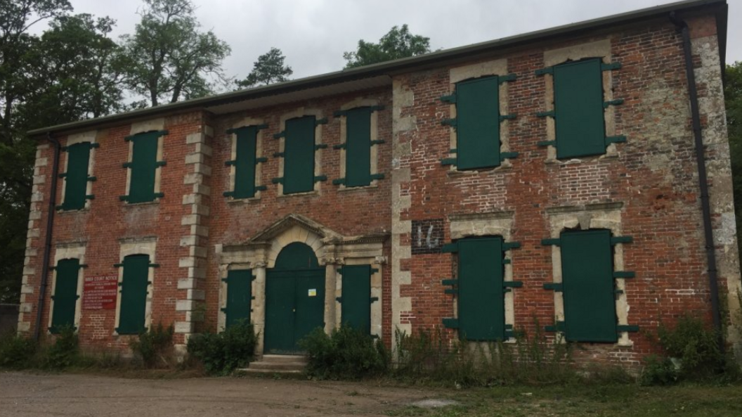 A derelict brick building with green coverings over its windows and doors to prevent access