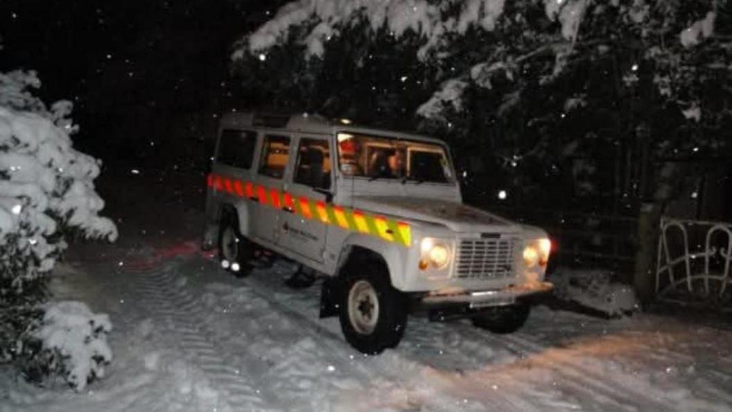 The picture shows a 4x4 vehicle in the dark on a snowy road.
