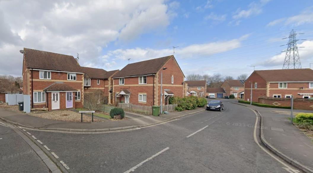 A street image of the road leading through Farriers Court, showing a road sign, homes and a black parked car.