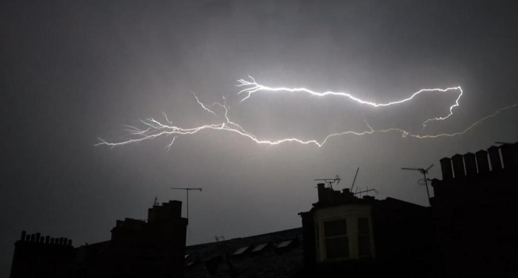 A dark night sky with the silhouette of buildings and a bright white lightning bolt in the sky