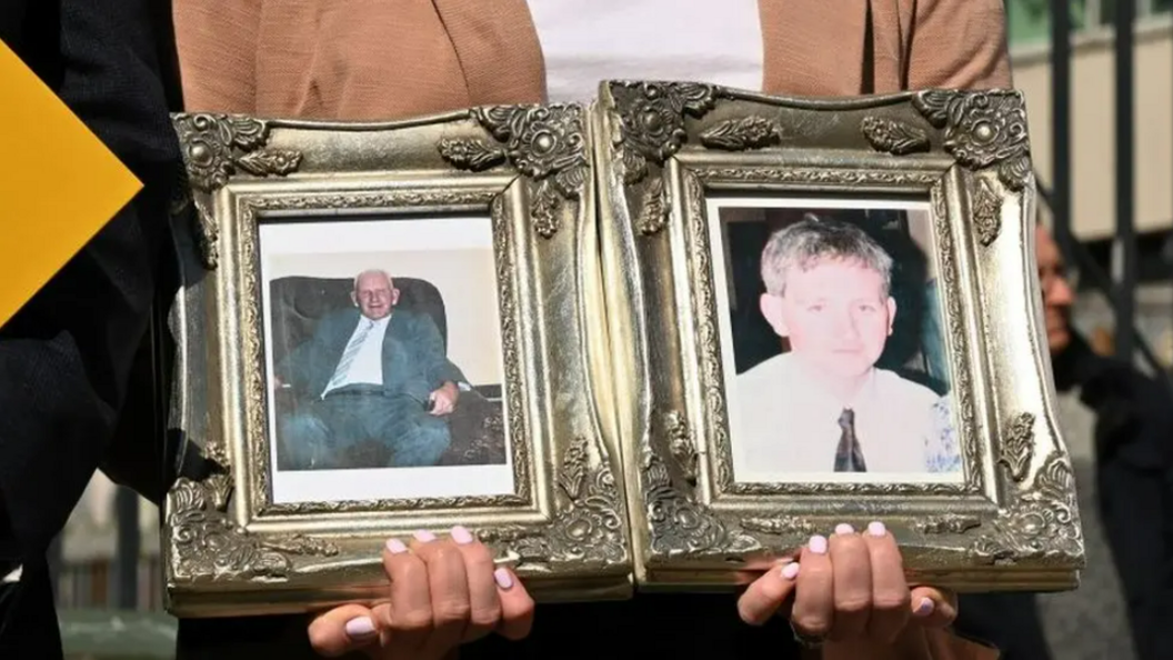 Hands holding two framed photos of two men - Kevin and John McKearney. The picture frames are gold and ornate.