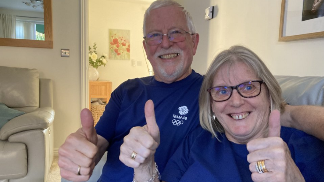 Meg Richards sits alongside husband Peter, sticking their thumbs up and smiling as they wear purple team GB shirts