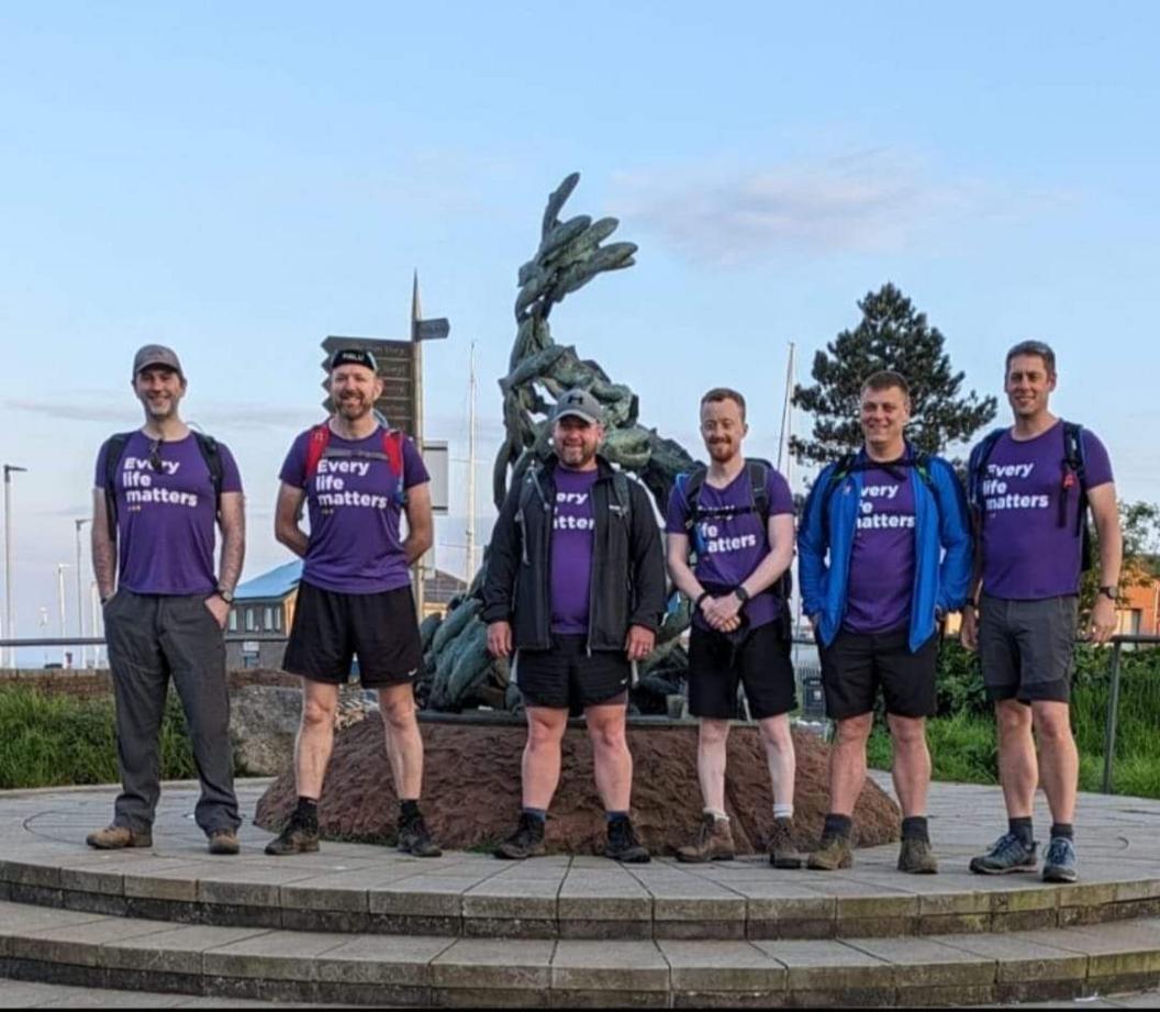 Six men stand in a row and are all wearing purple t-shirts which say 'Every Life Matters'