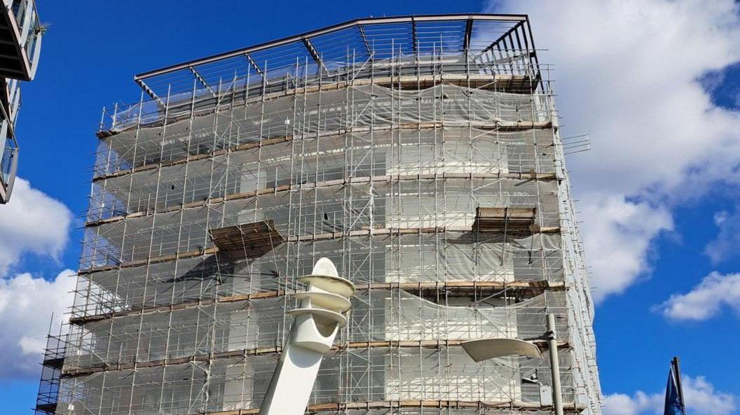 View looking up at the apartment block which is covered with scaffolding and netting