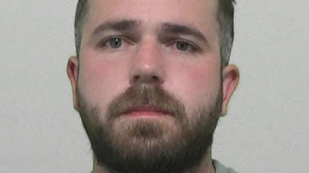 Mugshot of a young man with dark hair and a dark beard.