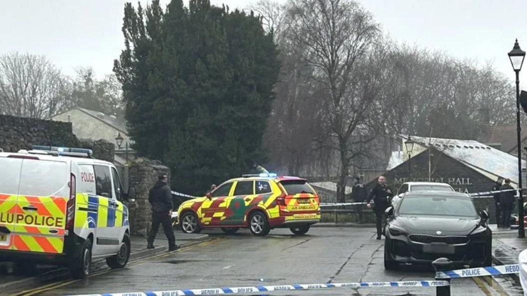 The scene outside the property in Llandaff, showing police officers and vehicles and a police cordon