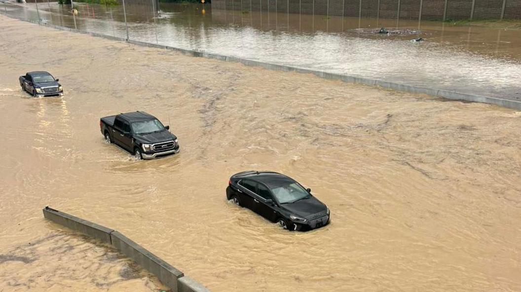 Two black trucks and a black crossover are seen surrounded by muddy brown water which is higher than their tires at points