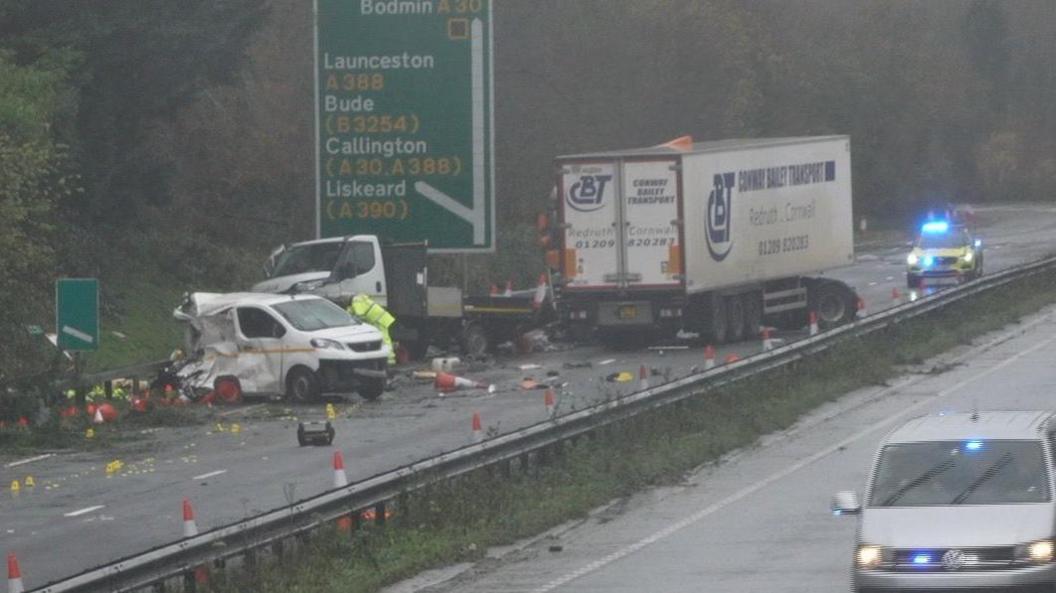 A picture of the scene showing crashed vehicles. A van looks partially crushed and there is debris across the road. 