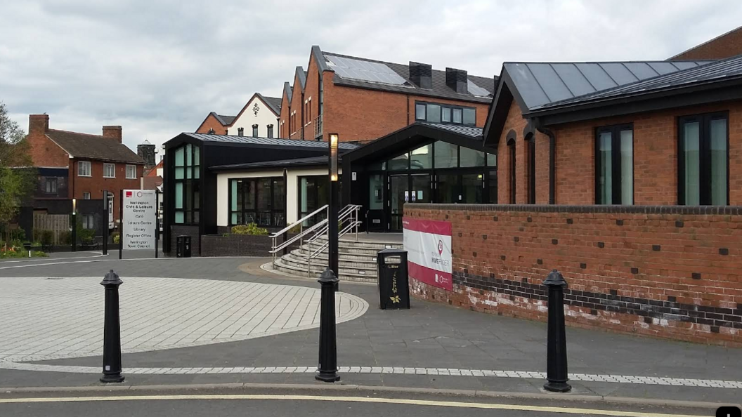 Wellington Civic Centre, a modern building with a paved area in front of it and steps leading up to the entrance. There are bollards between the paved area and the road.