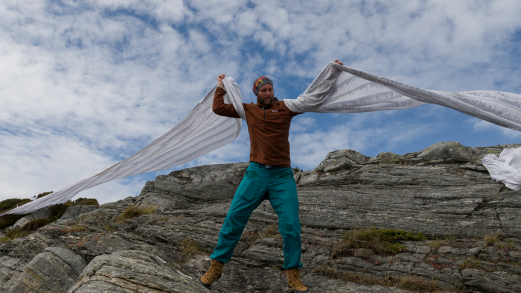 Tom Bailey standing on top of a mountain holding his arms aloft 