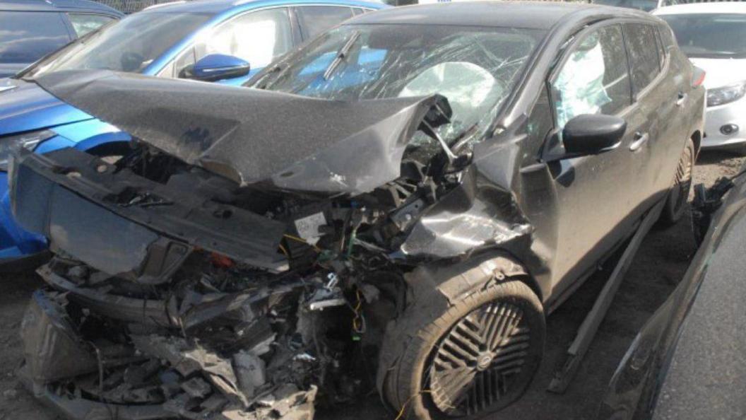 a black Nissan Leaf car with extensive damage to the hood and bumper, which are crumpled