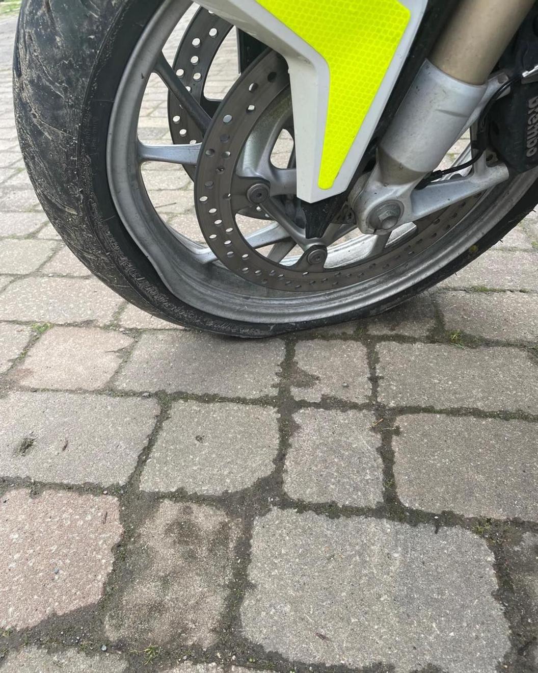 A close-up of a motorbike tyre which has deflated. The middle of the wheel is yellow to match the rest of the bike, and the tyre is on a bricked surface.