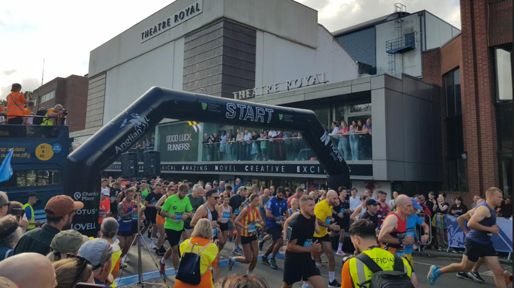 Runners passing over the start line outside Norwich Theatre Royal as spectators line the street