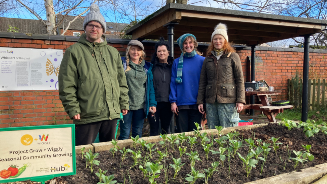 A photo of volunteers from the Wiggly Worm charity standing in front of a veg trough with plants growing inside