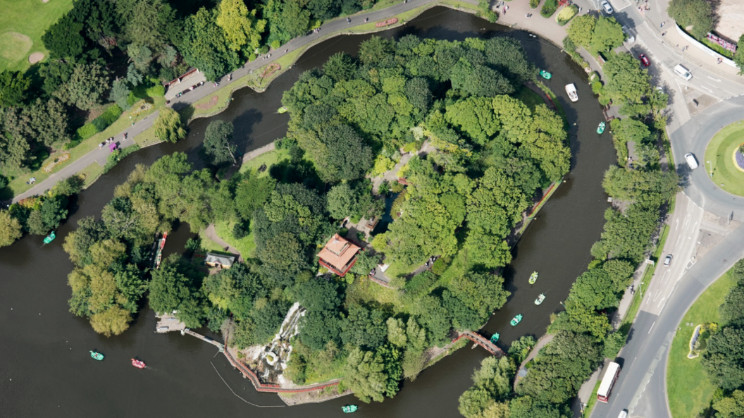 An aerial view of Peasholm Park in Scarborough. It shows a large lake, with an island in the middle. The island is covered in trees, with a red pagoda in the middle.