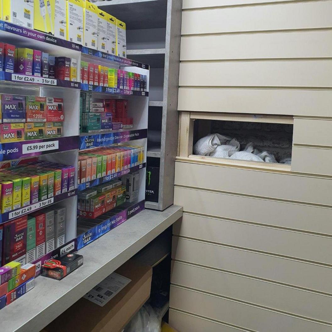 A secret compartment built into a wall of a shop. Inside the gap are bags filled with illegal tobacco products.
