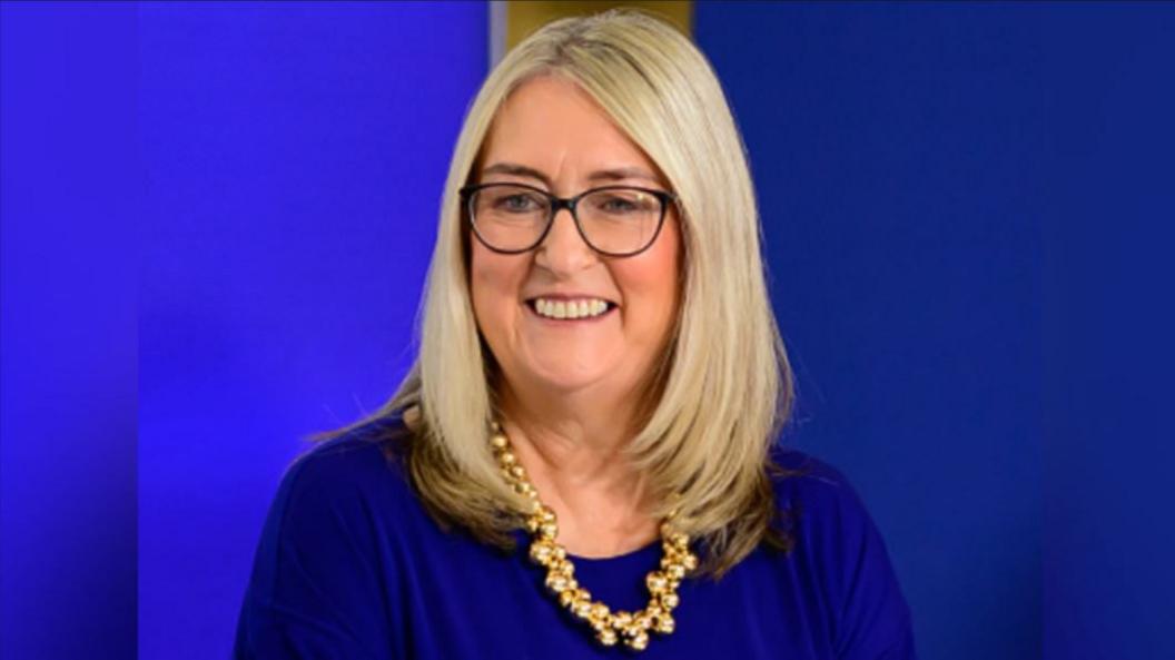 Baroness Jacqui Smith in a picture taken during an interview for a Labour Party conference. She is wearing a blue top and has a gold necklace. She has long blonde hair and is wearing glasses.