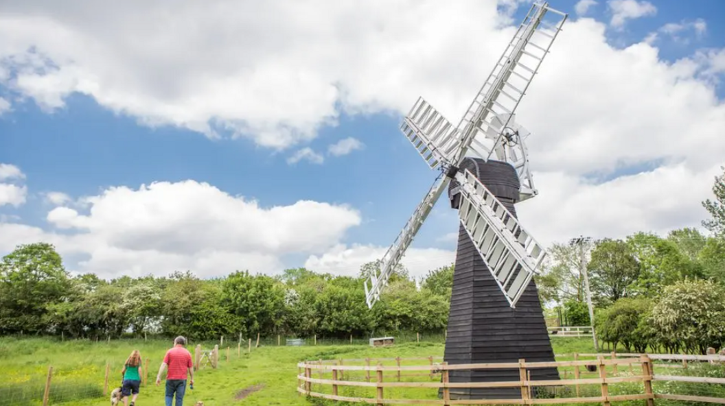 Two people walk next to a windmill in a field 