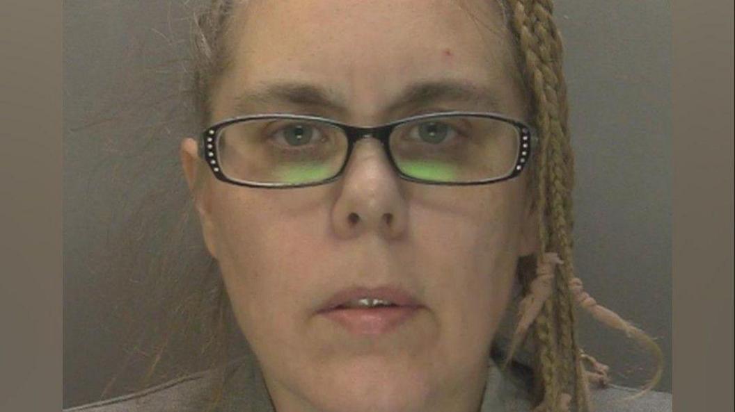Mugshot of Aimee Betro with plaits in her blonde hair and black glasses