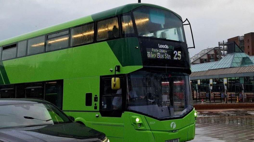 A green number 25 bus in Leeds city centre, en route to Ikley bus station. A black car is in the foreground. The city's bus station is in the background.