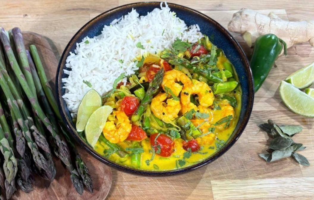 A picture of a curry cooked with prawns, coconut milk and seasonal British asparagus, garnished with sliced limes. 