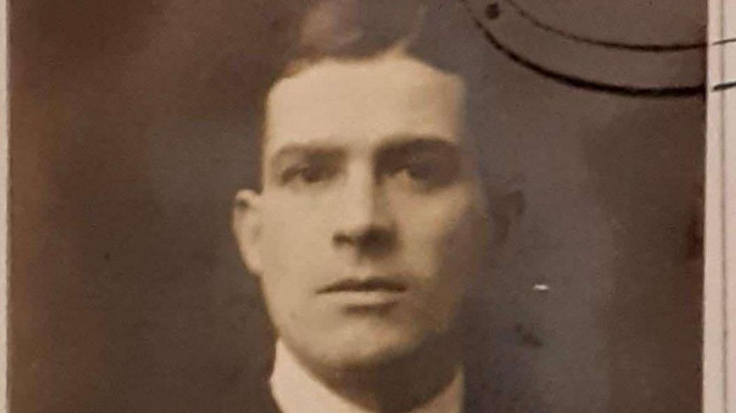 A sepia toned image of Frank Hills, he is looking directly at the camera, he wears a smart white collared shirt and has dark hair styled in a side parting