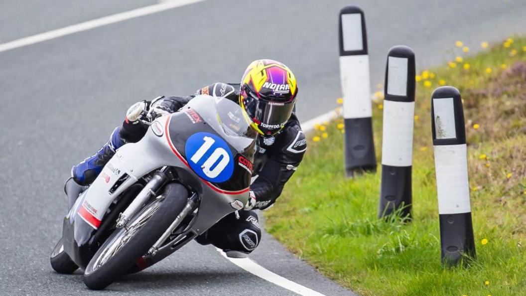 Paul Jordan on a silver and black machine with the number 10 in a blue plate on the front. His helmet is purple and yellow.