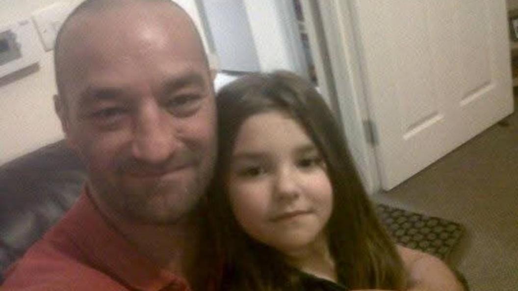 A picture of Lilli and her dad. The man on the left is smiling and wearing a red polo shirt. Lilli on the right has brown hair.