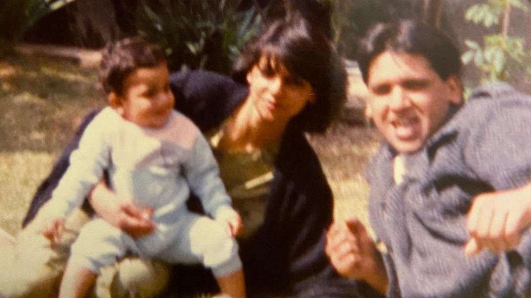 A dated home photo from the 1990s showing a young couple and their child on a lawn