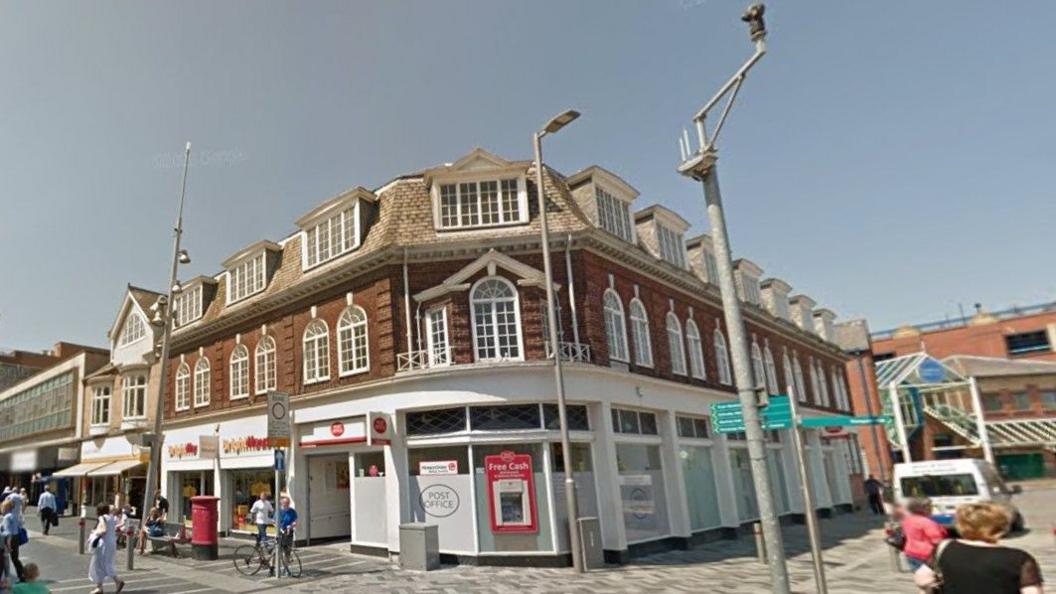 The Post Office in Grimsby. It is painted white and is a corner building. There is a cash machine to the front of the building.