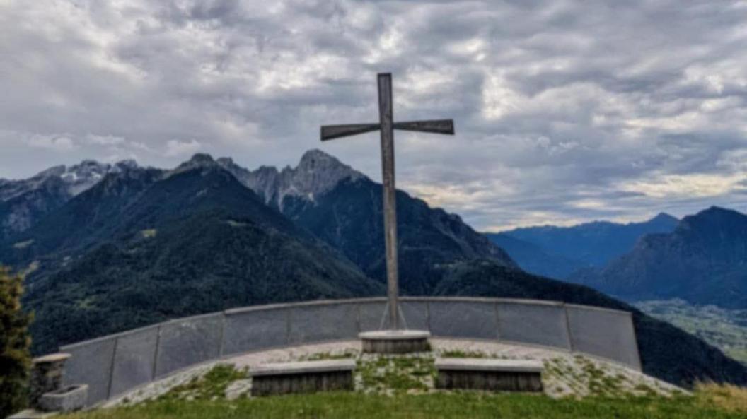 A large cross on top of a raised platform has a grey barrier in front of it. It overlooks several mountain tops on a cloudy day.