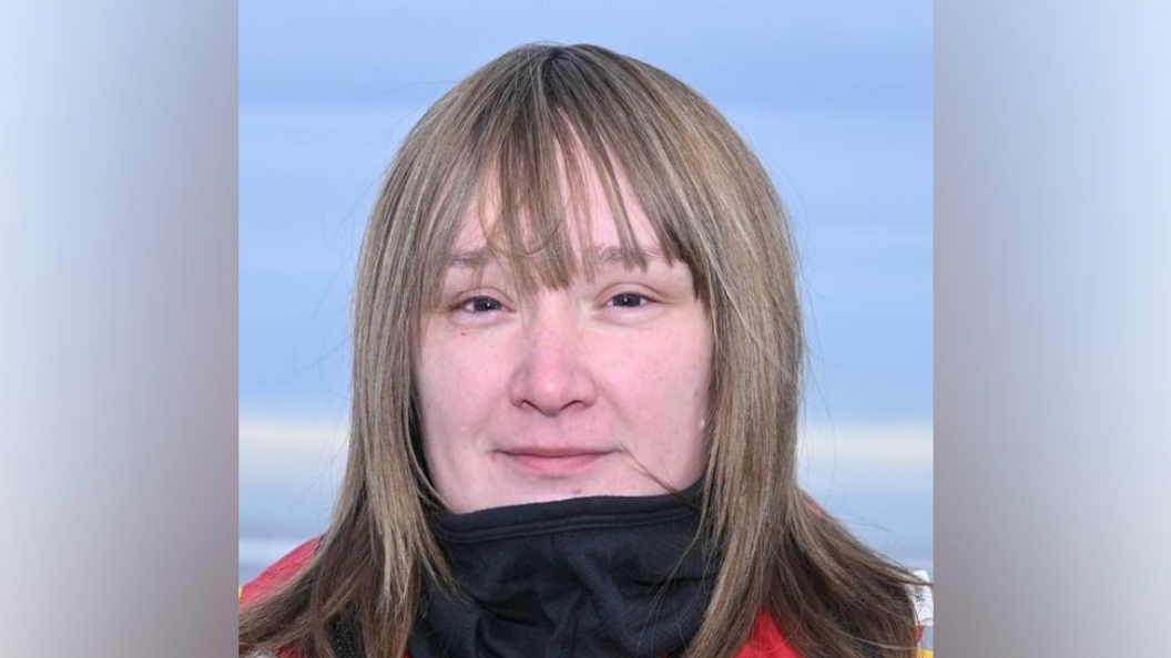 Laura Wedgewood with mid-length blonde/brown hair, with brown eyes, looks at the camera. She is wearing a red jacket and black snood.