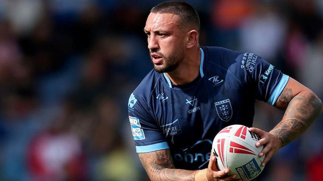 Elliot Minchella holds the ball in two hands, threatening to pass as he moves forward for Hull KR