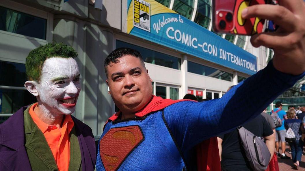 two smiling men having a selfie dressed as the Joker and Superman