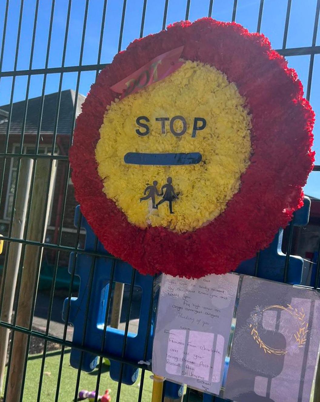 A red and yellow lollipop stick made out of artificial flowers, pinned to a green school fence.