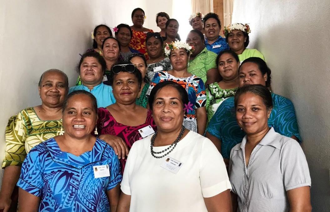 Dr Puakena Boreham, centre,  wearing white, surrounded by 20 women, all smiling, some in traditional Tuvaluan dress with flowers in their hair, in a photo from 2018