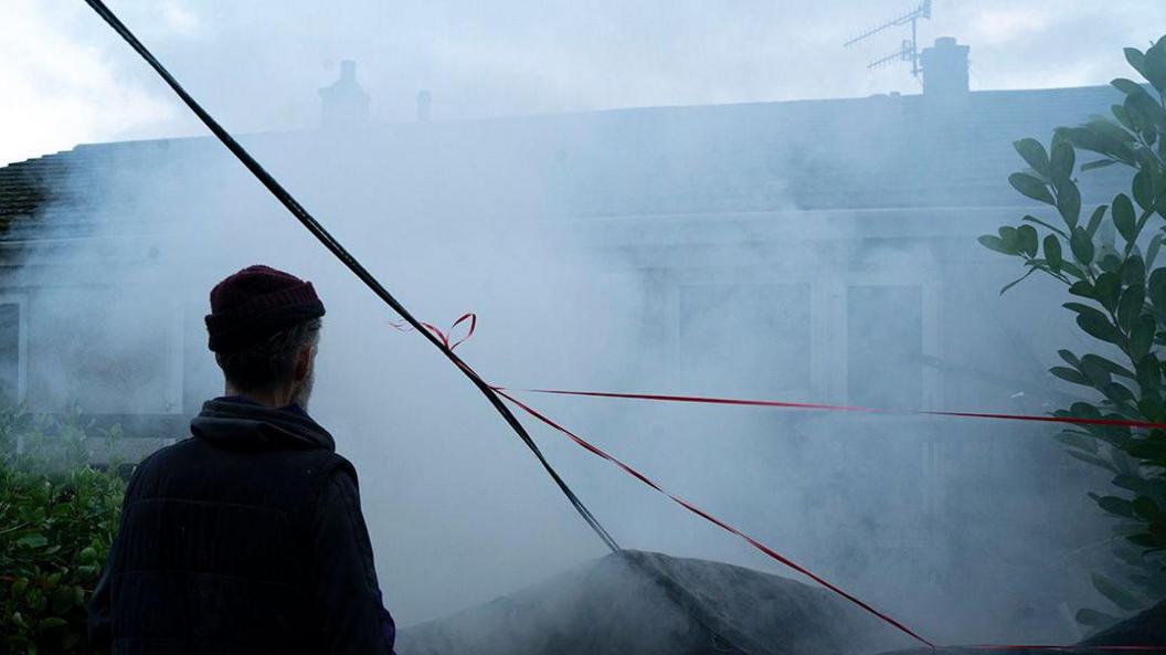 Tony looking at his house through smoke from the fire