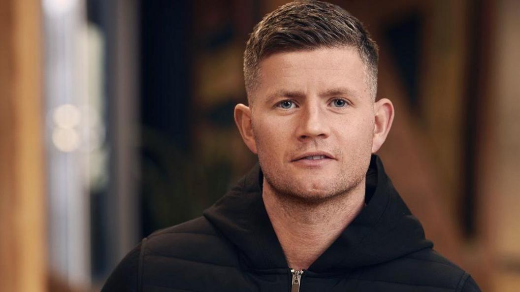 Tom Beahon is wearing a black hooded jacket and is staring at the camera in this posed image.