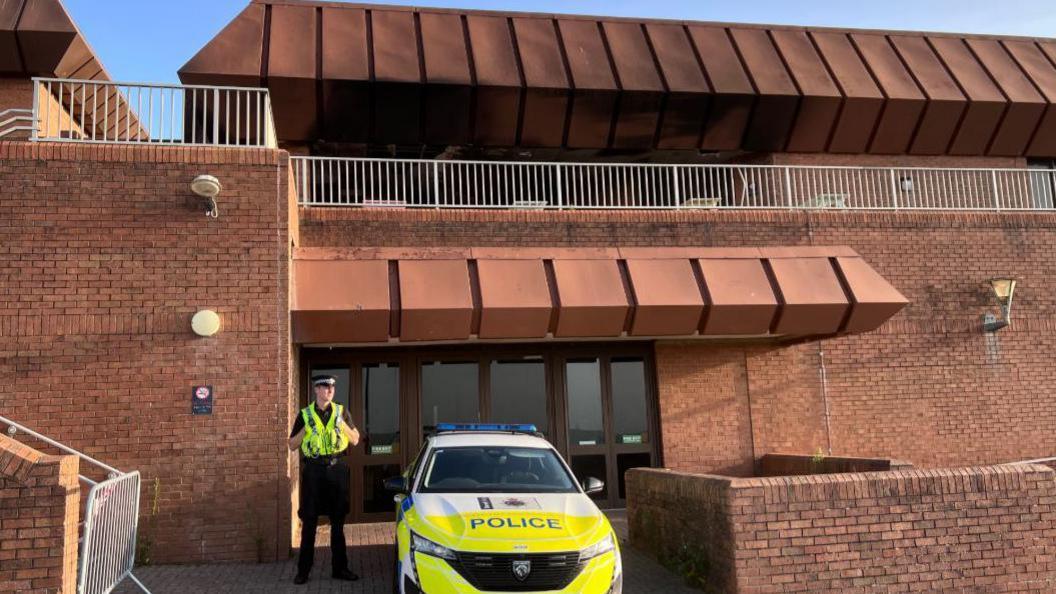 Police office standing beside a police car outside the Bournemouth International Centre.