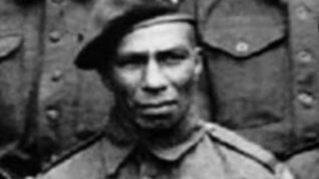 A black and white close-up photo of a man with a serious facial expression, frowning, wearing a soldiers suit and a beret.
