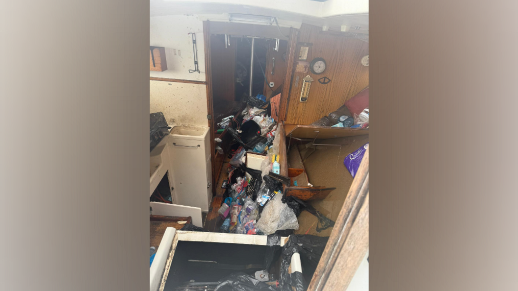 Rubbish and debris sit on a boat floor in a corridor. The room appears to show the kitchen of the boat filled with clutter from when the boat ran aground.