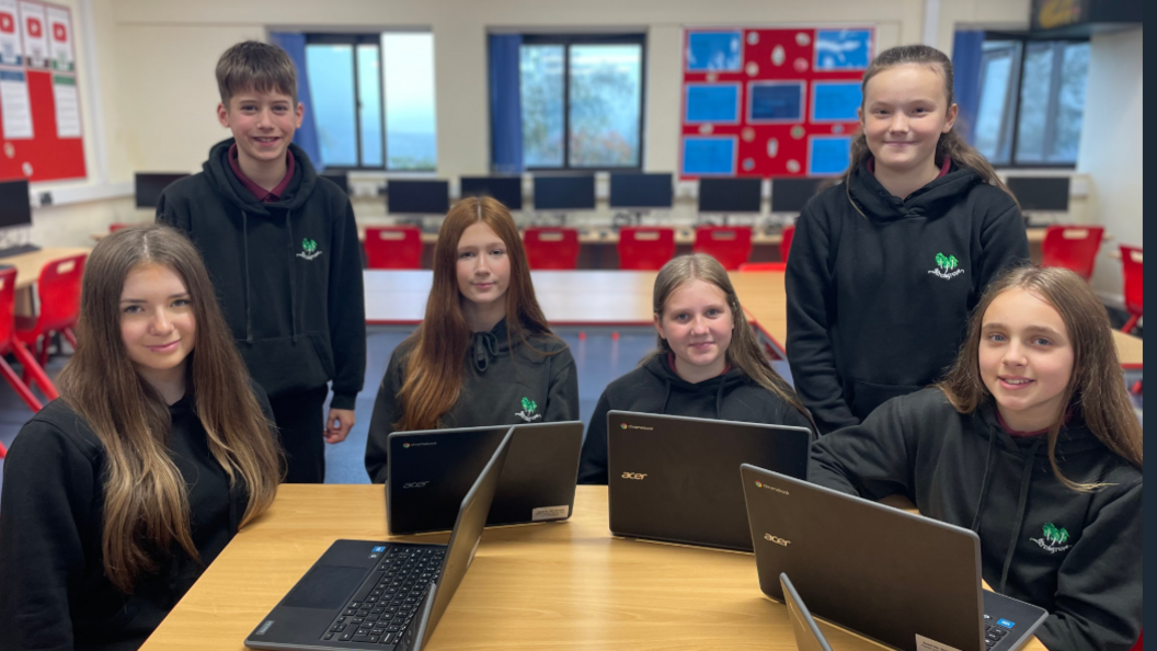 Pupils in a class at Birchgrove Comprehensive in Swansea sitting around a desk with their laptops open, five girls and and a boy.