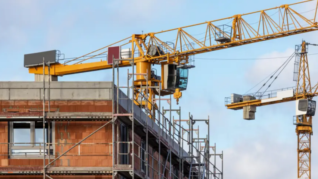 A stock image of housing being built. Two cranes can be seen alongside a housing development with scaffolding.