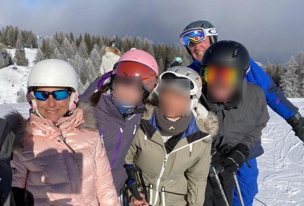A group of five people who are skiing with equipment and warm clothing on. Snow and trees can be seen behind them. 